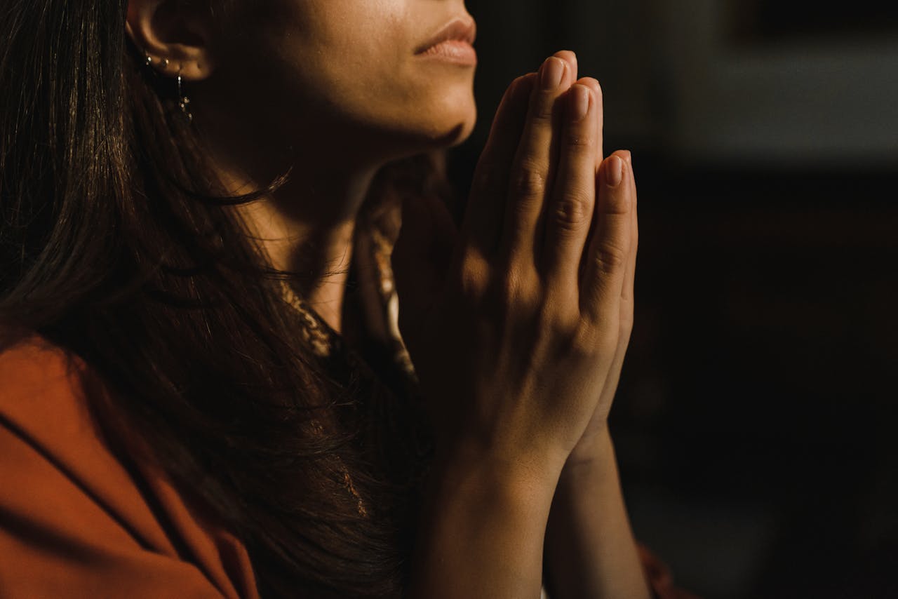 每日随读 Close-up of a woman with folded hands praying, captured in a serene indoor setting with low lighting.