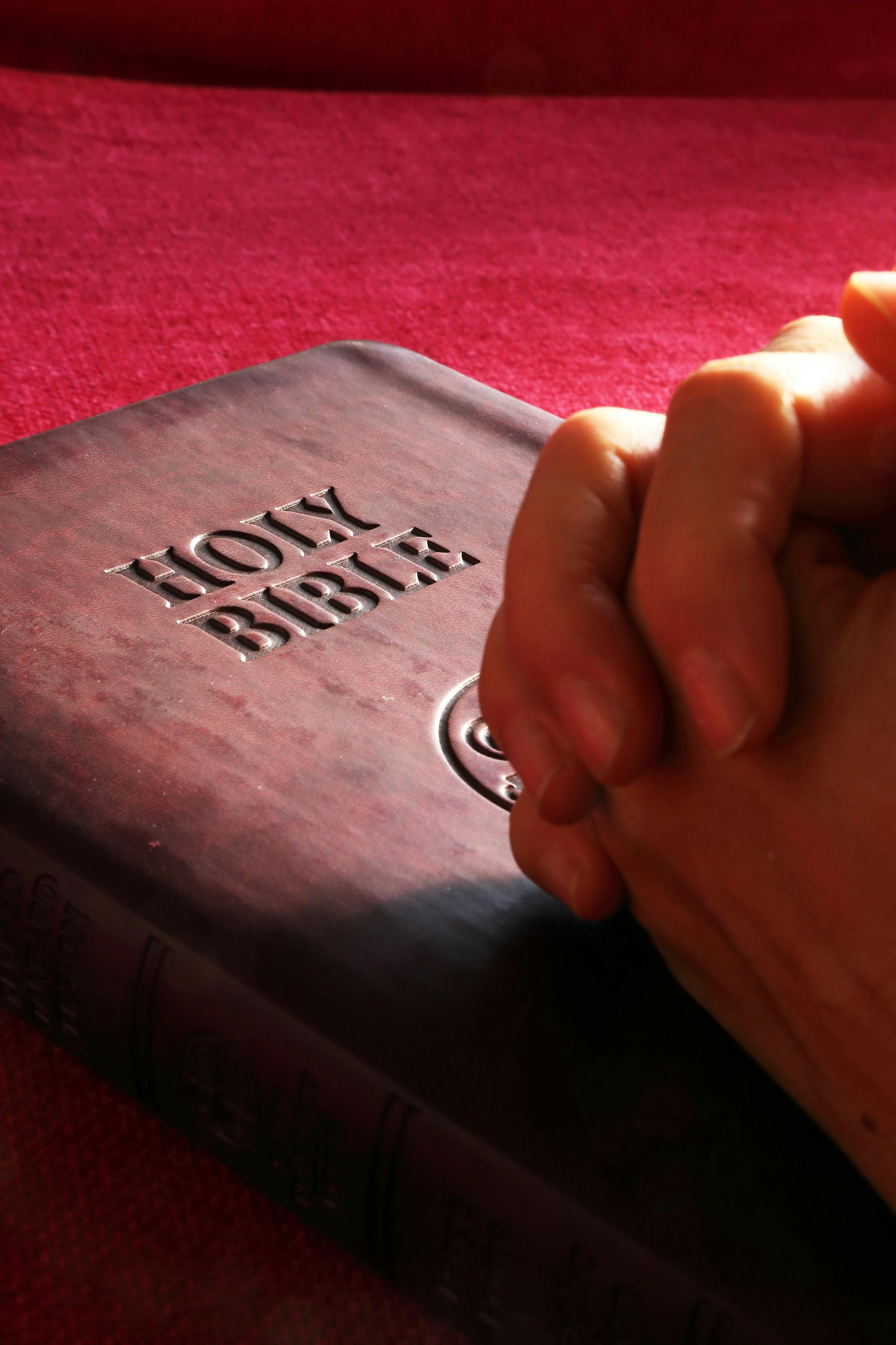 信仰的邀请 Close-up of hands praying on a Holy Bible, symbolizing faith and spirituality.